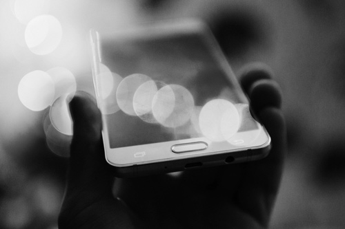 Bokeh effect photo of a hand holding a mobile device.